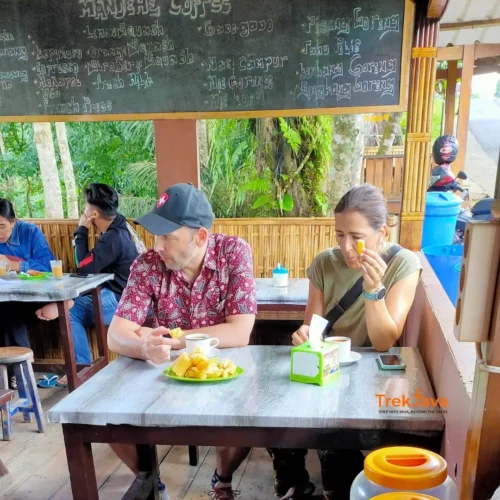 Two international travelers enjoying local coffee and traditional Banyuwangi snacks in East Java